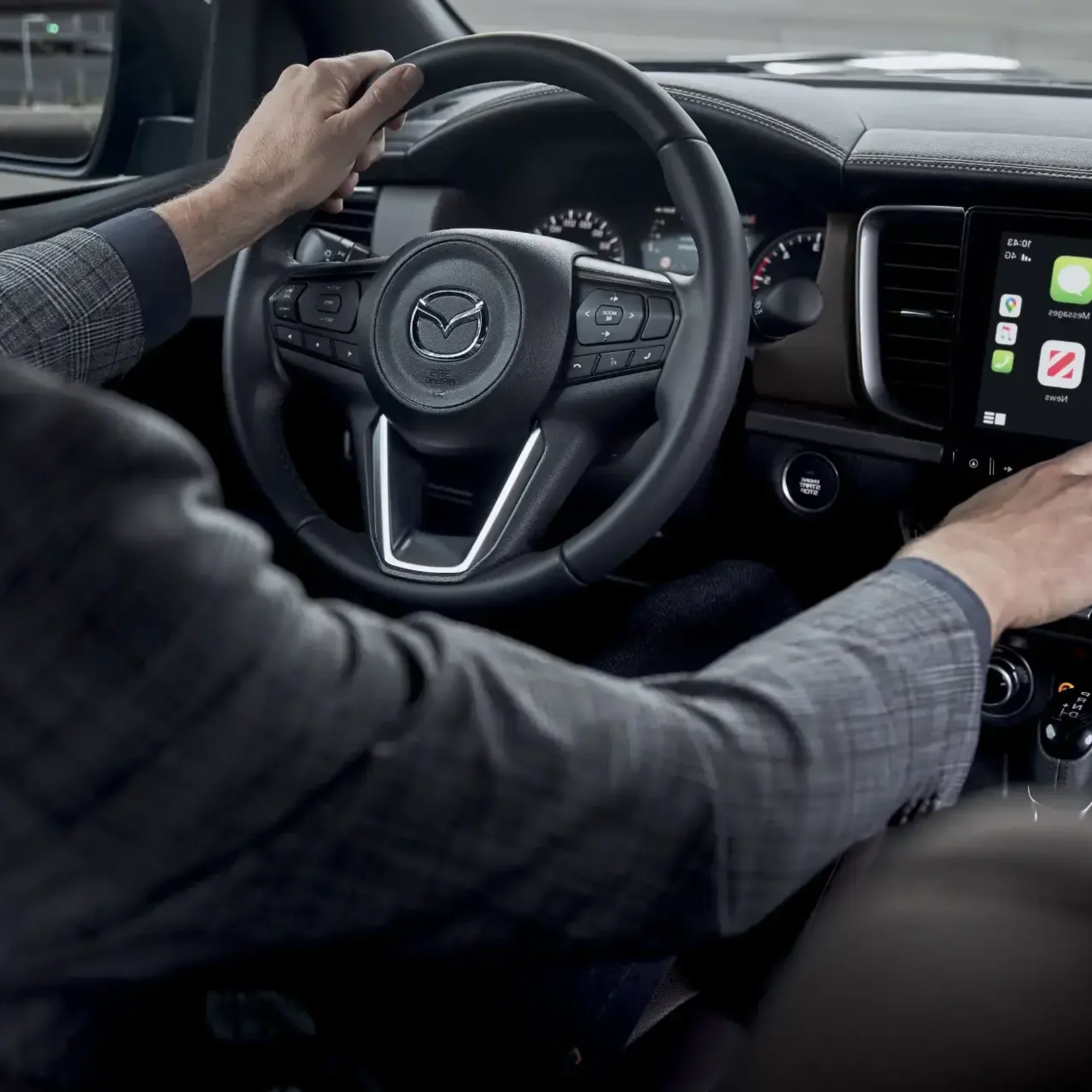 Hombre utilizando la pantalla táctil con Apple CarPlay en el interior de un Mazda, mostrando volante multifuncional y diseño moderno con acabados premium.