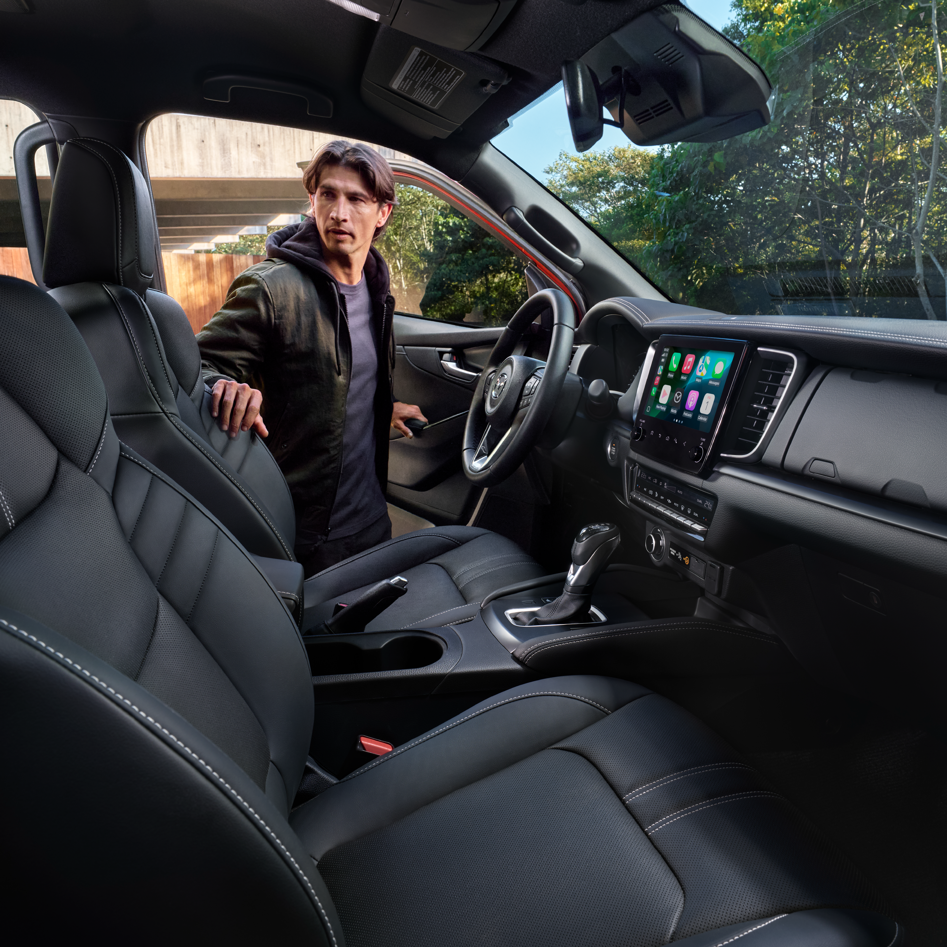 Conductor entrando a la Mazda BT-50 2025 con interior en piel y sistema Apple CarPlay en pantalla central.